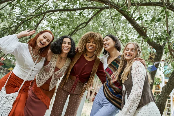 Trendy and interracial group of girlfriends looking at camera outdoors in retreat center — Stock Photo