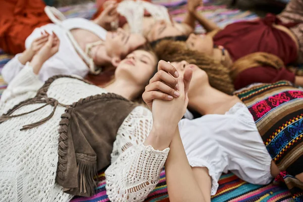 Blurred multiethnic women holding hands while lying on blanket outdoors in retreat center — Stock Photo