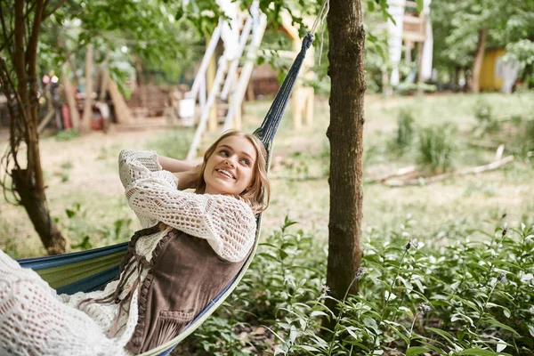 Jovem mulher loira alegre em roupas boho relaxante na rede no centro de retiro — Fotografia de Stock