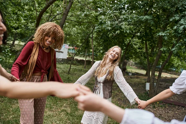 Happy multiethnic girlfriends in boho clothes holding hands and dancing in retreat center — Stock Photo