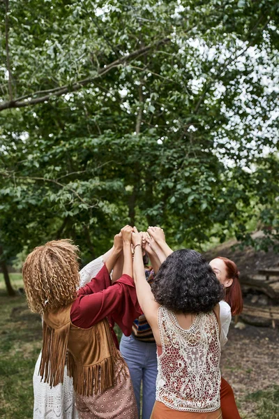 Trendy multiethnic girlfriends in boho clothes holding hands outdoors in retreat center — Stock Photo