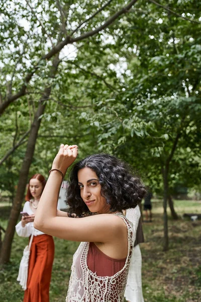 Smiling multiracial woman in boho outfit looking at camera on lawn in retreat center — Stock Photo