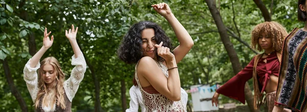Positive multiracial woman dancing near blurred girlfriends outdoors in retreat center, banner — Stock Photo