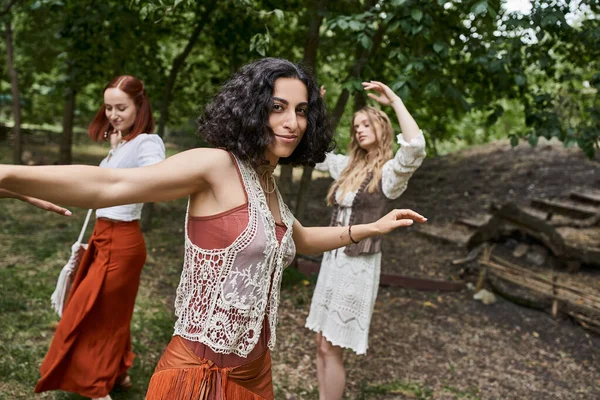 Trendy multiracial woman looking at camera and dancing near friends in modern retreat center — Stock Photo