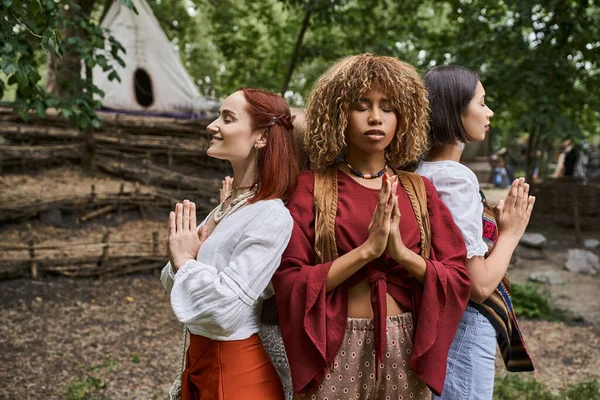 Multiethnic women with closed eyes doing praying hands gesture outdoors in retreat center — Stock Photo