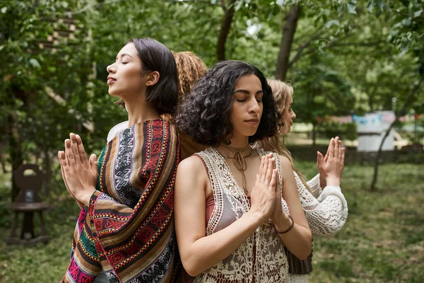Multiracial woman with closed eyes doing praying hands gesture near friends in retreat center — Stock Photo