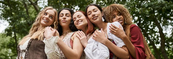 Vista a basso angolo di donne interrazziali positive in abiti boho che si abbracciano nel centro della ritirata, banner — Foto stock