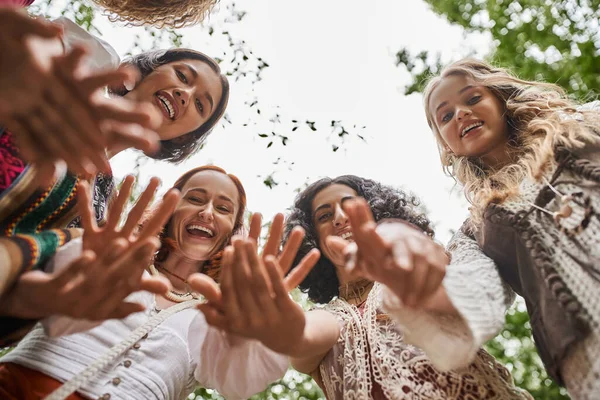 Bottom view of positive and trendy interracial women waving at camera in retreat center — Stock Photo