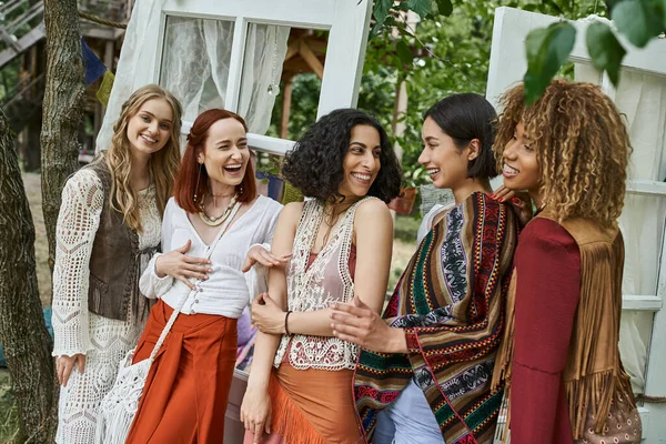 Mulheres multiétnicas alegres em roupas boho falando enquanto em pé no centro de retiro moderno — Fotografia de Stock