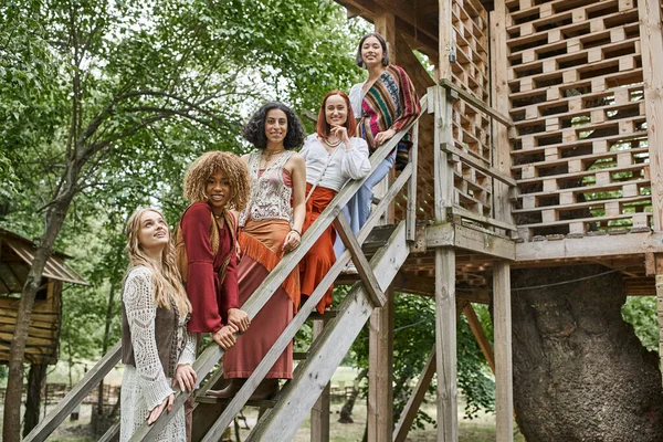 Glückliche multiethnische Freundinnen in trendigen Boho-Klamotten stehen auf der Treppe des Retreat-Zentrums — Stockfoto