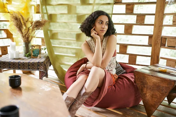 Mulher multirracial sonhadora e positiva em roupas estilo boho sentado no saco de feijão no centro de retiro — Fotografia de Stock