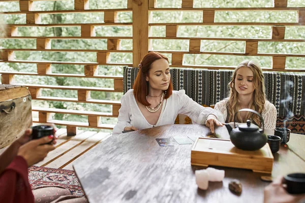 Женщина читает карты Таро рядом с подругами, сидя за деревянным столом, гармонии и спокойствия — стоковое фото