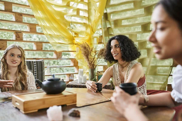 Women retreat concept, multiracial woman drinking tea with girlfriends at wooden table — Stock Photo
