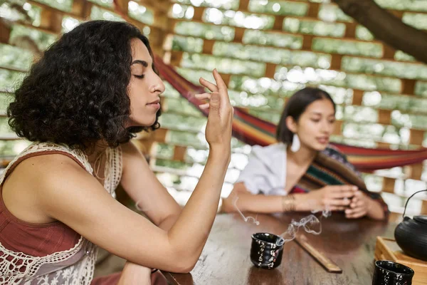 Multiracial woman enjoying palo santo flavor near cup of tea, relaxation, harmony — Stock Photo