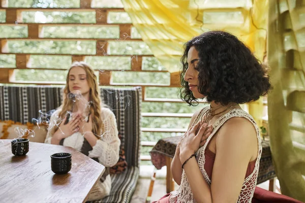 Multiethnische Freundinnen mit geschlossenen Augen meditieren mit Palo Santo-Geschmack in der Nähe von Teetassen — Stockfoto