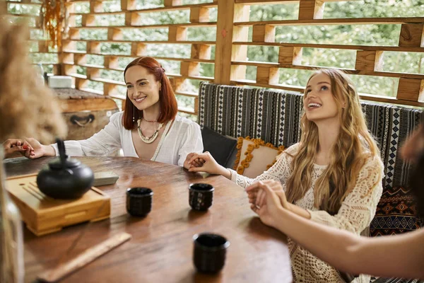 Women retreat, carefree girlfriends meditating and holding hands near tea cups on wooden table — Stock Photo