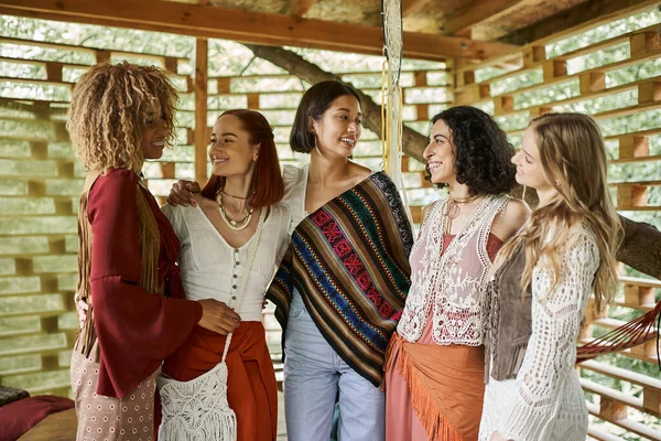 Women retreat, happy multiethnic girlfriends in boho style outfit looking at each other in cottage — Stock Photo