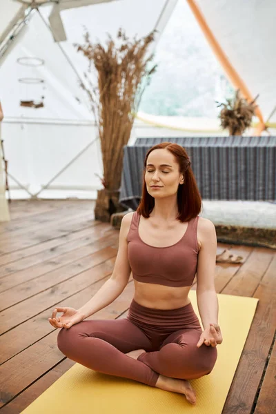 Donna in abbigliamento sportivo meditando in posa di loto con gli occhi chiusi nel centro di ritiro, tranquillità — Foto stock