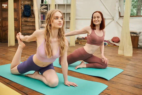 Молодые девушки в спортивной одежде практикующие йогу в голубиной позе в современном ретритном центре — стоковое фото