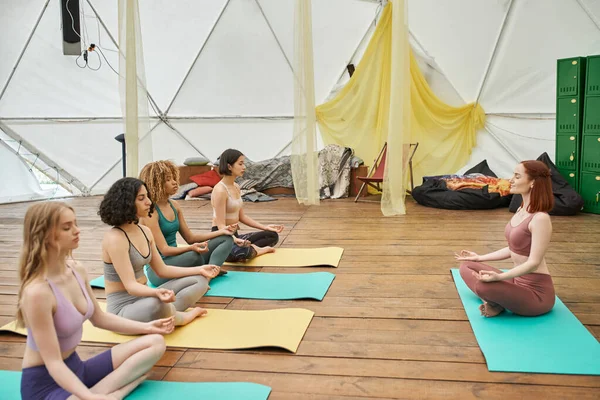 Concepto de retiro de mujeres, mujeres multiétnicas en ropa deportiva meditando en postura de yoga sobre alfombras de yoga - foto de stock