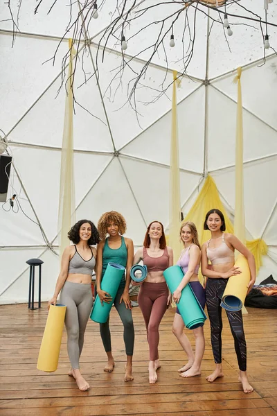Estilo de vida saudável, mulheres multiétnicas alegres em sportswear, com tapetes de ioga no centro de retiro moderno — Fotografia de Stock