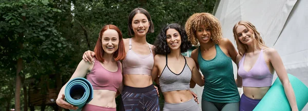Rückzugskonzept für Frauen, zufriedene multiethnische Freundinnen mit Yogamatten, die im Park in die Kamera schauen — Stockfoto