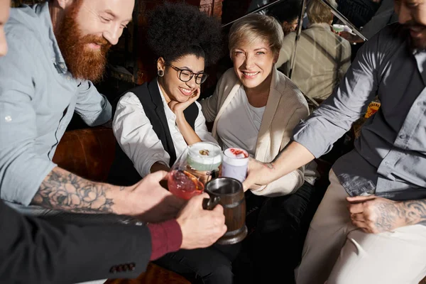 Alegres colegas multiétnicos tintineando vasos con cócteles mientras se divierten en el bar después del trabajo - foto de stock