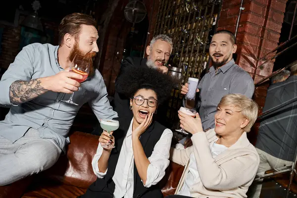 Mujer africana emocionada riendo cerca de amigos de trabajo multicultural relajarse con cócteles en el bar - foto de stock