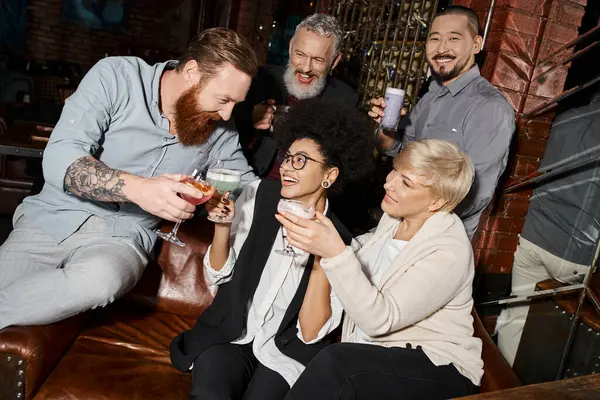 Бородатий татуйований чоловік смердить окуляри з багатоетнічними жінками поблизу усміхнених робочих однокласників у коктейльному барі — стокове фото