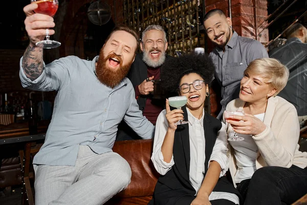 Схвильовані багатоетнічні друзі тримають напої і сміються в коктейльному барі, розважаючись після роботи — стокове фото