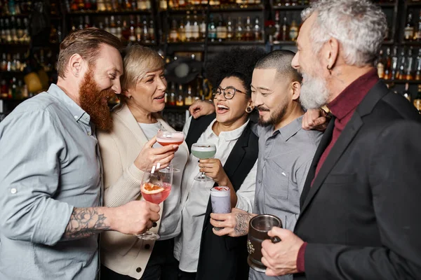 Joyful multicultural colleagues holding glasses with drinks and talking in cocktail bar after work — Stock Photo