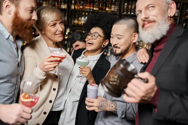 Excited african american woman with cocktail laughing near multiethnic workmates relaxing in bar — Stock Photo