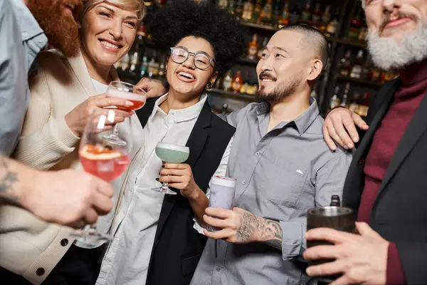 Усміхнені багатоетнічні колеги тримають окуляри з алкогольними напоями, проводячи час у барі — стокове фото