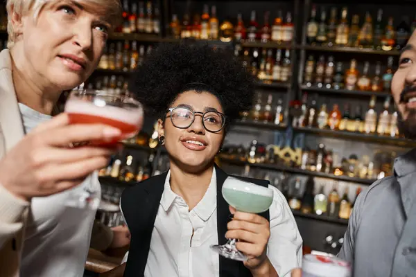 Donna afro-americana sorridente vicino a amici di lavoro multietnici che tengono da bere e parlano nel bar — Foto stock