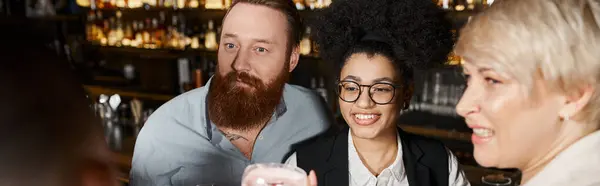 Surprised bearded man near cheerful multiethnic women spending after work time in cocktail bar — Stock Photo
