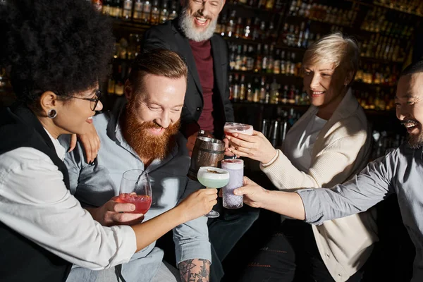 Разнообразная команда веселых мультикультурных друзей, звонящих в стаканы, развлекаясь в коктейль-баре — стоковое фото