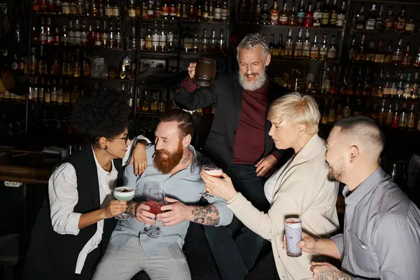 Alegre afroamericano mujer y barbudo hombre hablando cerca multiétnico compañeros de trabajo con bebidas en bar - foto de stock