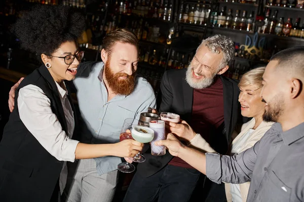 Hombres barbudos y mujeres felices tintineo vasos en el bar, después del ocio de trabajo de colegas multiétnicos - foto de stock