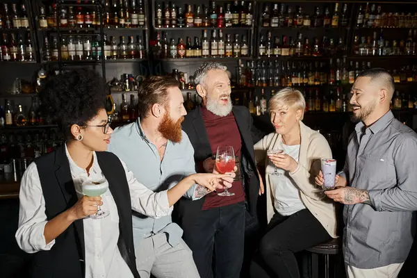 Femme d'âge moyen regardant la caméra près d'amis multiculturels positifs boire des cocktails dans le bar — Photo de stock