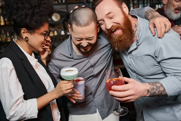 Hombres barbudos excitados y mujer afroamericana riendo en el bar, ocio de compañeros de trabajo multiétnicos - foto de stock