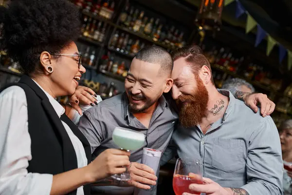 Бородаті чоловіки та афроамериканка сміються в коктейльному барі, відпочивають багатоетнічні колеги — стокове фото