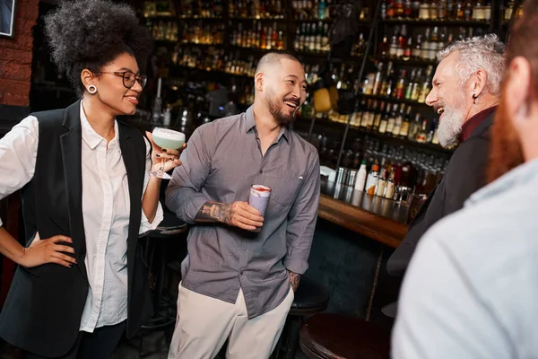 African american woman with cocktail smiling near bearded multiethnic colleagues talking in bar — Stock Photo