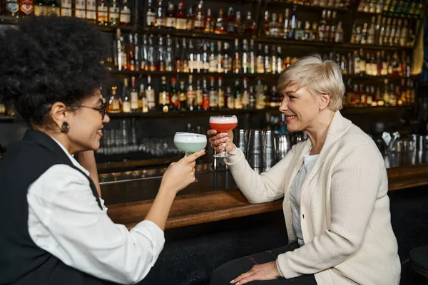 Smiling multiethnic women toasting with cocktails glasses while spending time in bar after work — Stock Photo