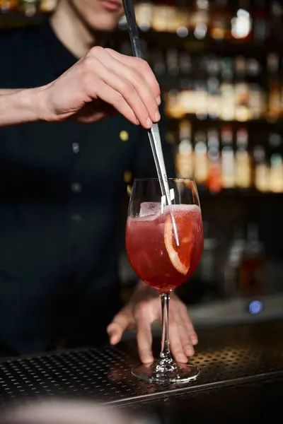 Vue recadrée du barman en ajoutant une tranche d'orange fraîche dans un cocktail alcoolisé au bar, création de boissons — Photo de stock