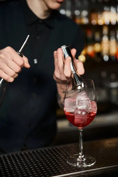 Артистизм коктейлей, обрезанный вид бармена, добавляющего кубики льда в фруктовый коктейль на барной стойке — стоковое фото