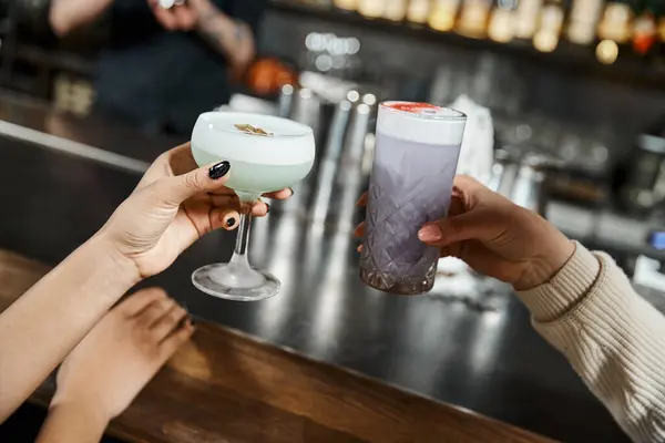 Cropped view of multiethnic female colleagues holding delicious cocktails in bar after work — Stock Photo