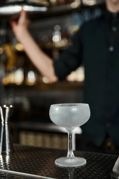 Verre à cocktail congelé préparé pour la fabrication de cocktails près de barman cultivé sur fond flou — Photo de stock