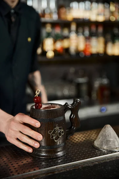 Cropped view of bartender near wooden mug with craft Kriek cocktail in bar, mixology artistry — Stock Photo