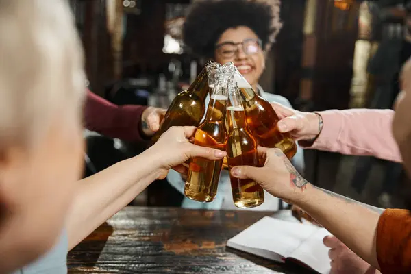 Multicultural business people relaxing in pub after work and clinking beer bottles, happy time — Stock Photo