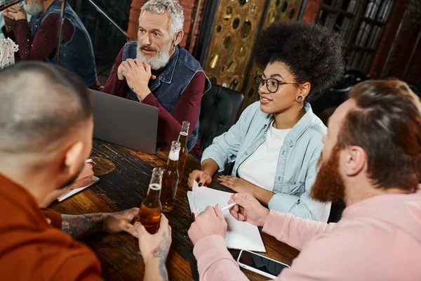 Multiethnic business colleagues sitting in pub near laptop while planning new startup project — Stock Photo